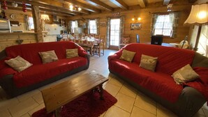 Un interior de cabaña acogedor con dos sofás rojos, una mesa de comedor de madera y una zona de cocina.