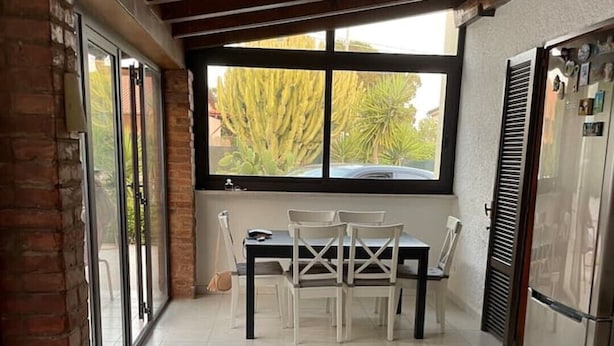 A dining area with a table and chairs, a window with a view of trees, and a refrigerator. - Vacation home Andreina (the yellow) (Ognina)