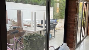 A covered patio area with a brick wall, a large sliding glass door, and a view of a backyard with a table, chairs, and a bicycle. - Vacation home Andreina (the yellow) (Ognina)