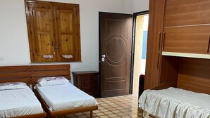 A room with two single beds, a wooden wardrobe, a door, and a tiled floor. - Vacation home Andreina (the yellow) (Ognina)