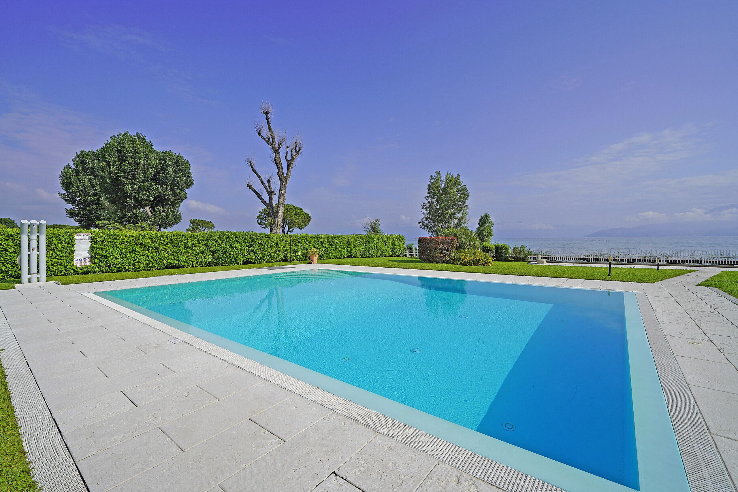 A rectangular swimming pool with a clear blue water surface, surrounded by a paved deck.