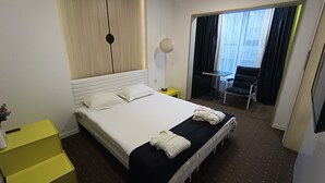 A hotel room with a large bed, a small table, a chair, and a view of the outside through a window. - IO hotel Bishkek (Bishkek)