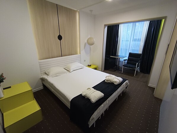 A hotel room with a large bed, a small table, a chair, and a view of the outside through a window.