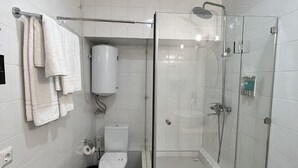 A modern bathroom with white tiles, a glass-enclosed shower, a toilet, and a towel rack. - IO hotel Bishkek (Bishkek)