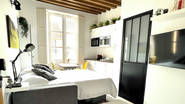 Une chambre d’hôtel de taille réduite, comprenant un lit, une table de chevet, une lampe et un coin cuisine équipé d’un four à micro-ondes et d’un réfrigérateur.