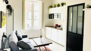 Une cuisine moderne avec des meubles blancs, un réfrigérateur noir et une fenêtre équipée de stores.