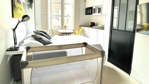 Une chambre d’hôtel compacte comprenant un lit, une lampe de chevet, une petite table et une chaise. Elle dispose également d’une kitchenette équipée d’un four à micro-ondes et d’un réfrigérateur.