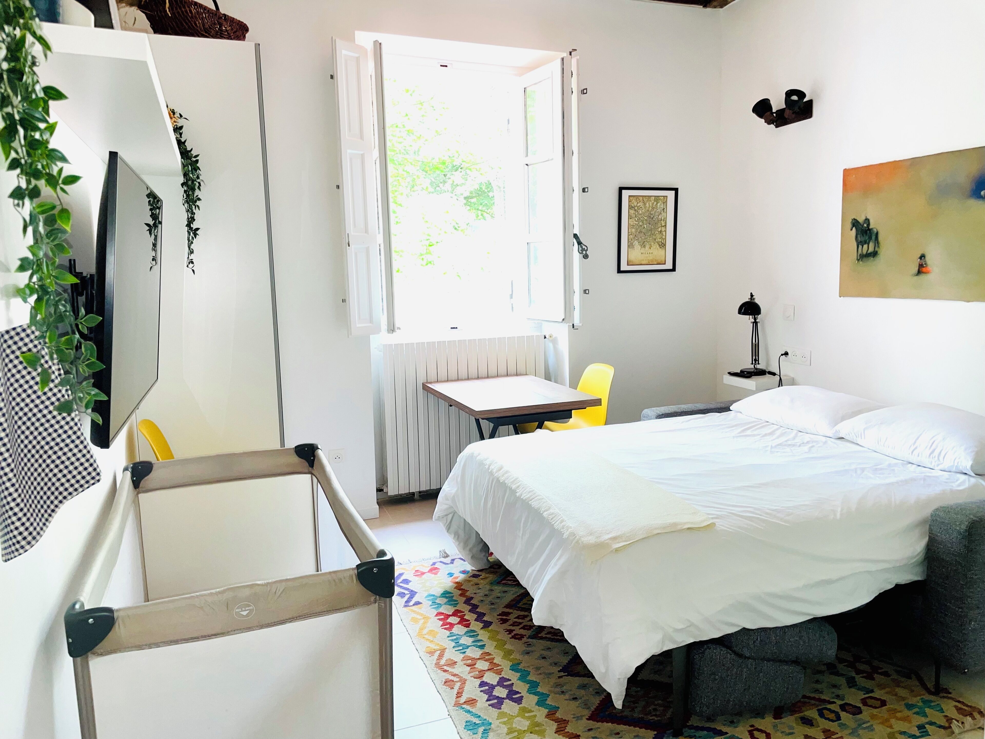 A room with a bed, a desk, a chair, a radiator, a window, and a painting on the wall.