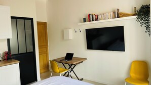 Un dormitorio moderno con cama, escritorio con computadora portátil, televisor y estantería.