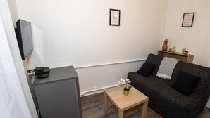 Ein kompakter Wohnbereich mit Sofa, kleinem Tisch, einem an einem Schrank montierten Fernseher und zwei gerahmten Bildern an der Wand.