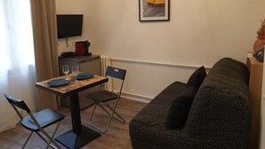 Ein kompakter Wohnbereich mit Esstisch, zwei Stühlen, einer Couch, einem an der Wand montierten Fernseher und einem gerahmten Bild über der Couch.