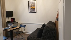 Ein kleiner, möblierter Raum mit einer Couch, einem Esstisch mit Stühlen, einem Flachbildfernseher und einem gerahmten Bild an der Wand.