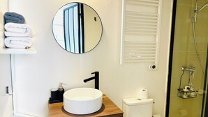 Et badeværelse med et rundt spejl, en vask med træbordplade, toilet og en bruseniche.