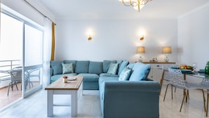 Un soggiorno moderno con un divano componibile, un tavolino da caffè, una zona pranzo con un tavolo in vetro e sedie, e un balcone con poltrone in vimini.