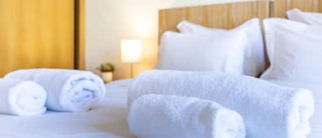 A neatly made bed with rolled white towels and a wooden headboard.