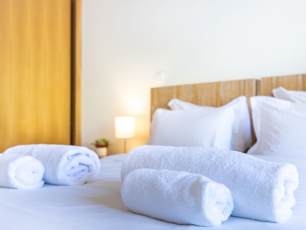 A neatly made bed with rolled white towels and a wooden headboard.