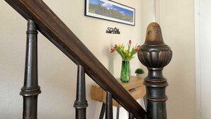 A wooden staircase with a dark finish, a framed landscape photo on the wall, and a small green vase with flowers on a wooden table.