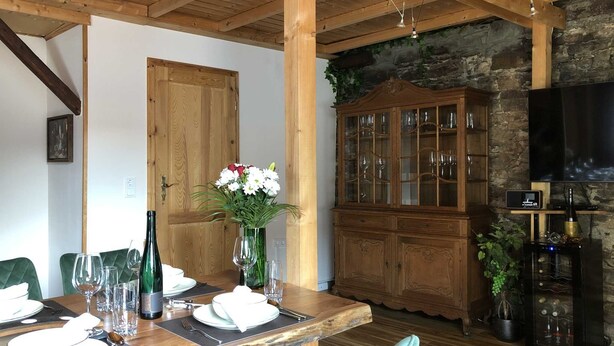A dining area with a wooden table set for a meal, a cabinet with glassware, and a television on the wall.