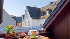A balcony with a table set for a meal, including a cake, fruit, and a bottle of water.