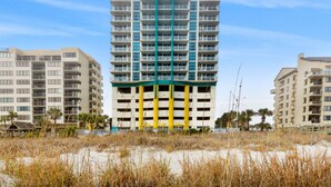 Un hôtel à plusieurs étages, doté de balcons, situé près d’une plage bordée de dunes de sable.
