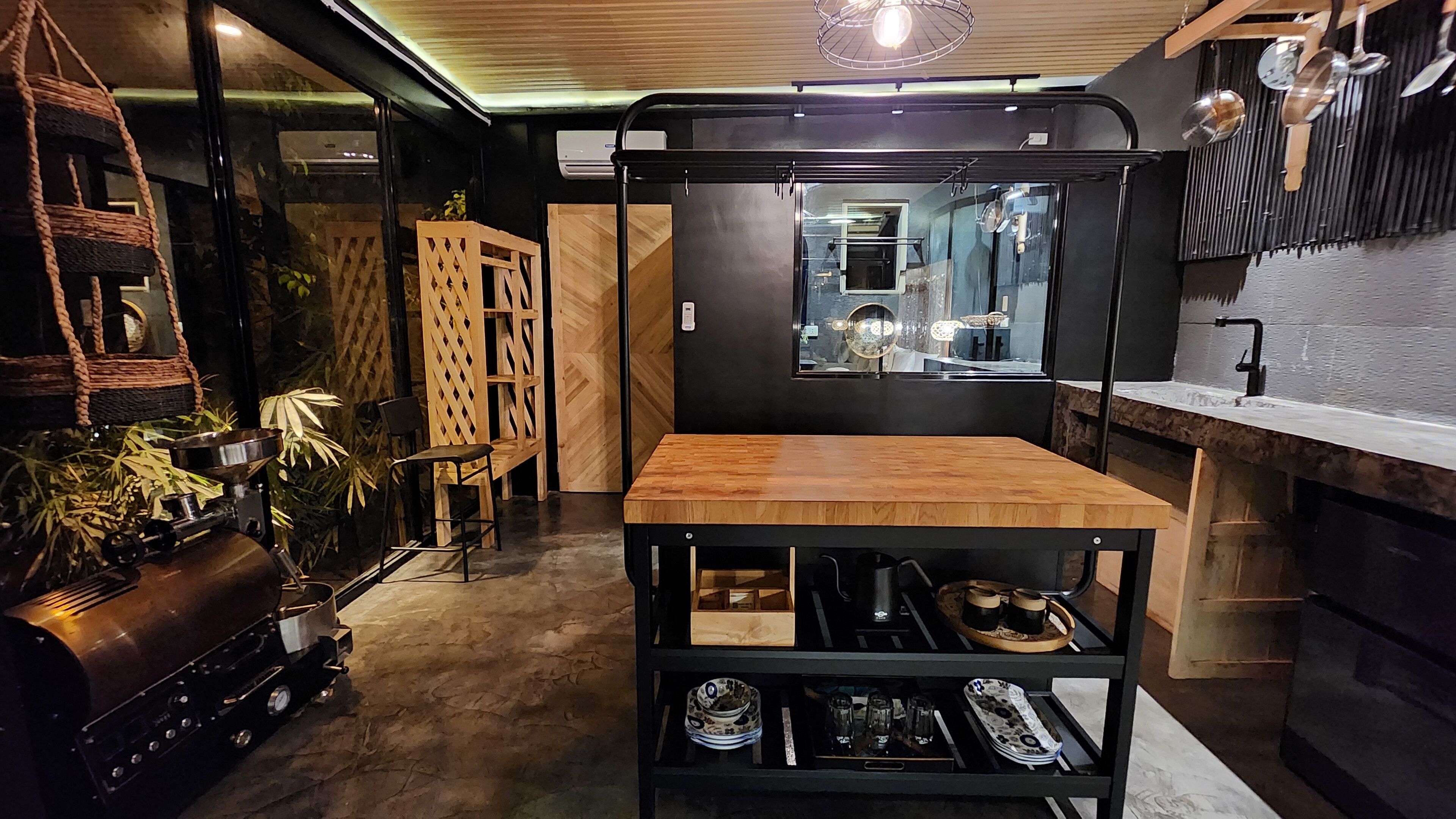 A compact kitchen with a wooden table, black shelving, and a hanging pot rack.