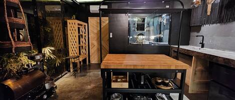 A compact kitchen with a wooden table, black shelving, and a hanging pot rack.