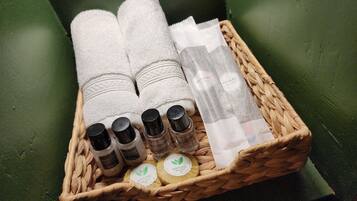 A wicker basket containing various toiletries including bottles of shampoo, body wash, and bath soap, along with a dental kit and a white towel.