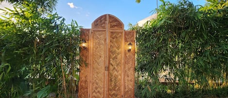 A wooden gate with a herringbone pattern, flanked by lush greenery and two wall-mounted lights.