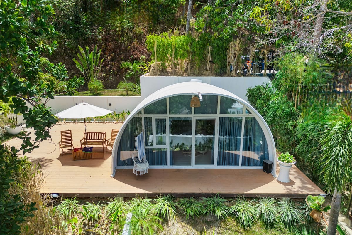 Ein modernes Haus mit einem großen Glasfenster, einer Holzterrasse und Gartenmöbeln.