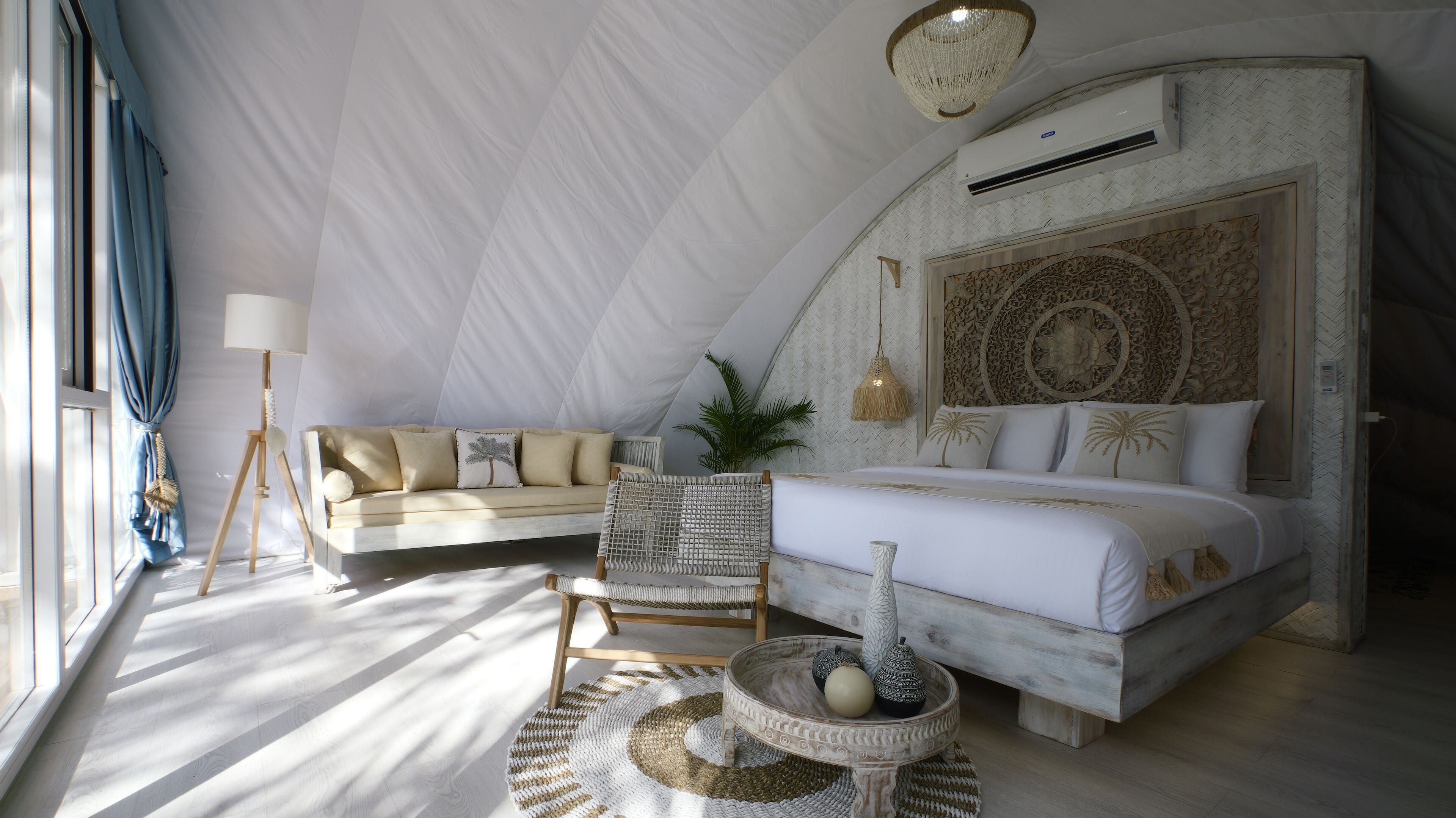 A spacious bedroom with a large bed, a sofa, a wicker chair, and a small table with decorative items.