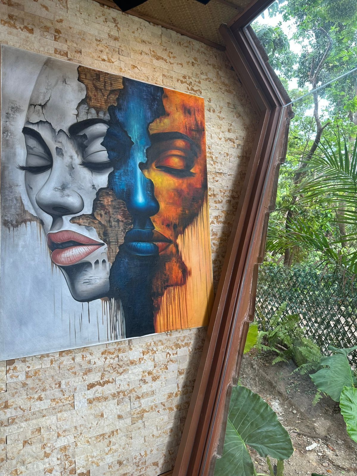 Un mur orné d’un grand tableau abstrait et une fenêtre donnant sur un espace verdoyant.