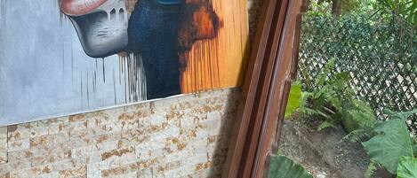 Un mur orné d’un grand tableau abstrait et une fenêtre donnant sur un espace verdoyant.