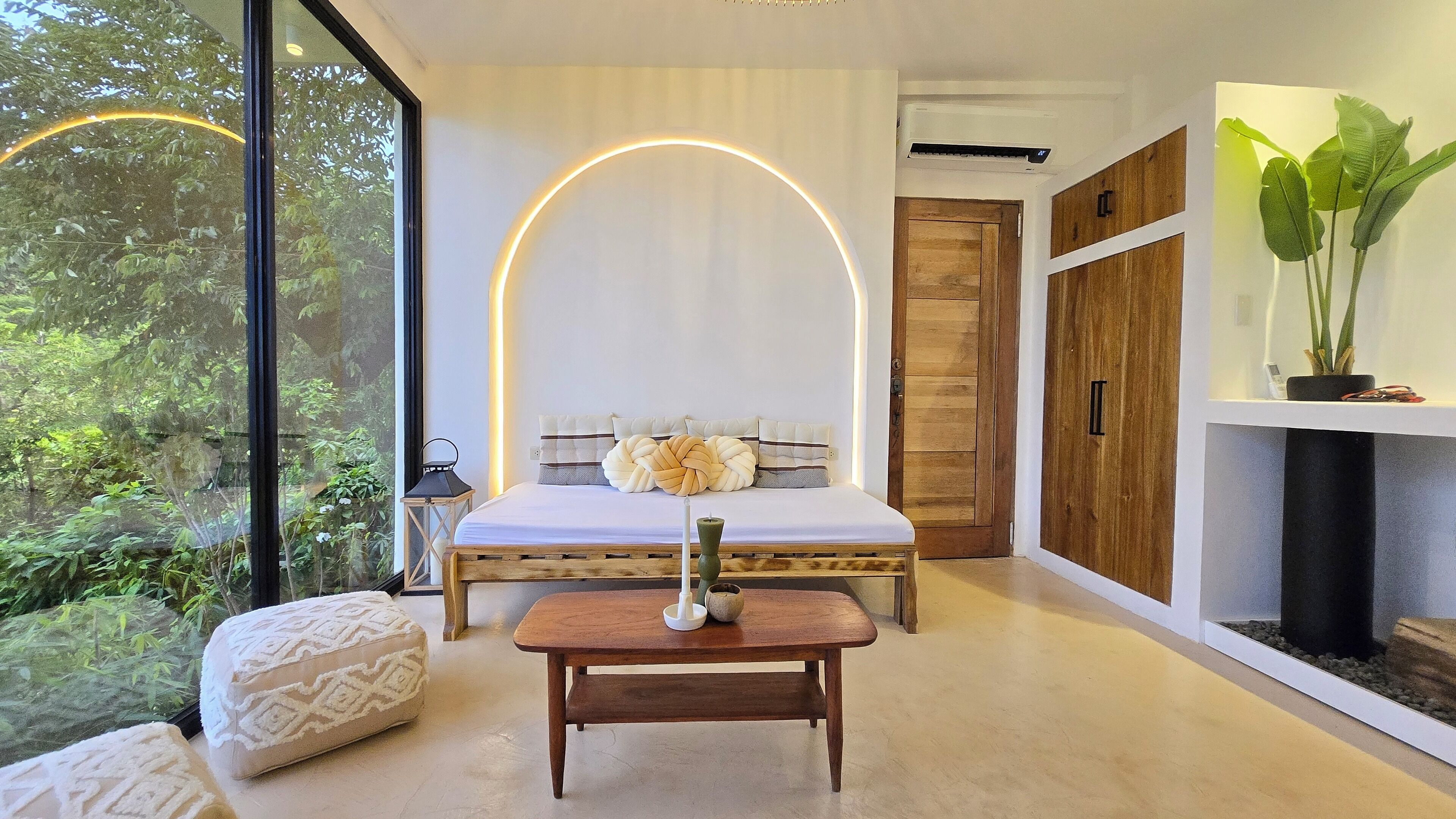 Un dormitorio con cama, mesita de noche y vistas a la vegetación a través de amplios ventanales.