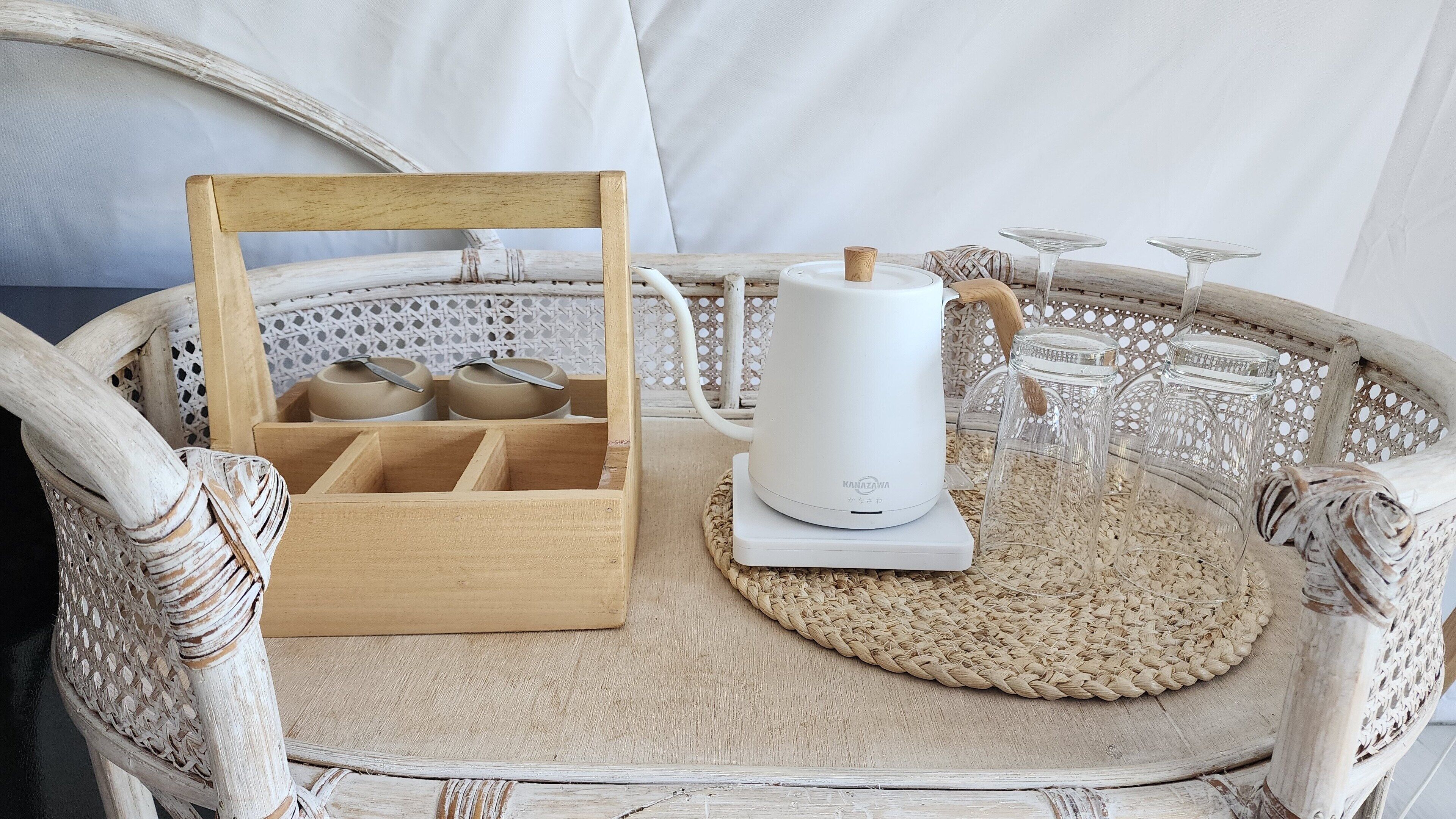 A wicker tray with a white electric kettle and a wooden basket containing jars.