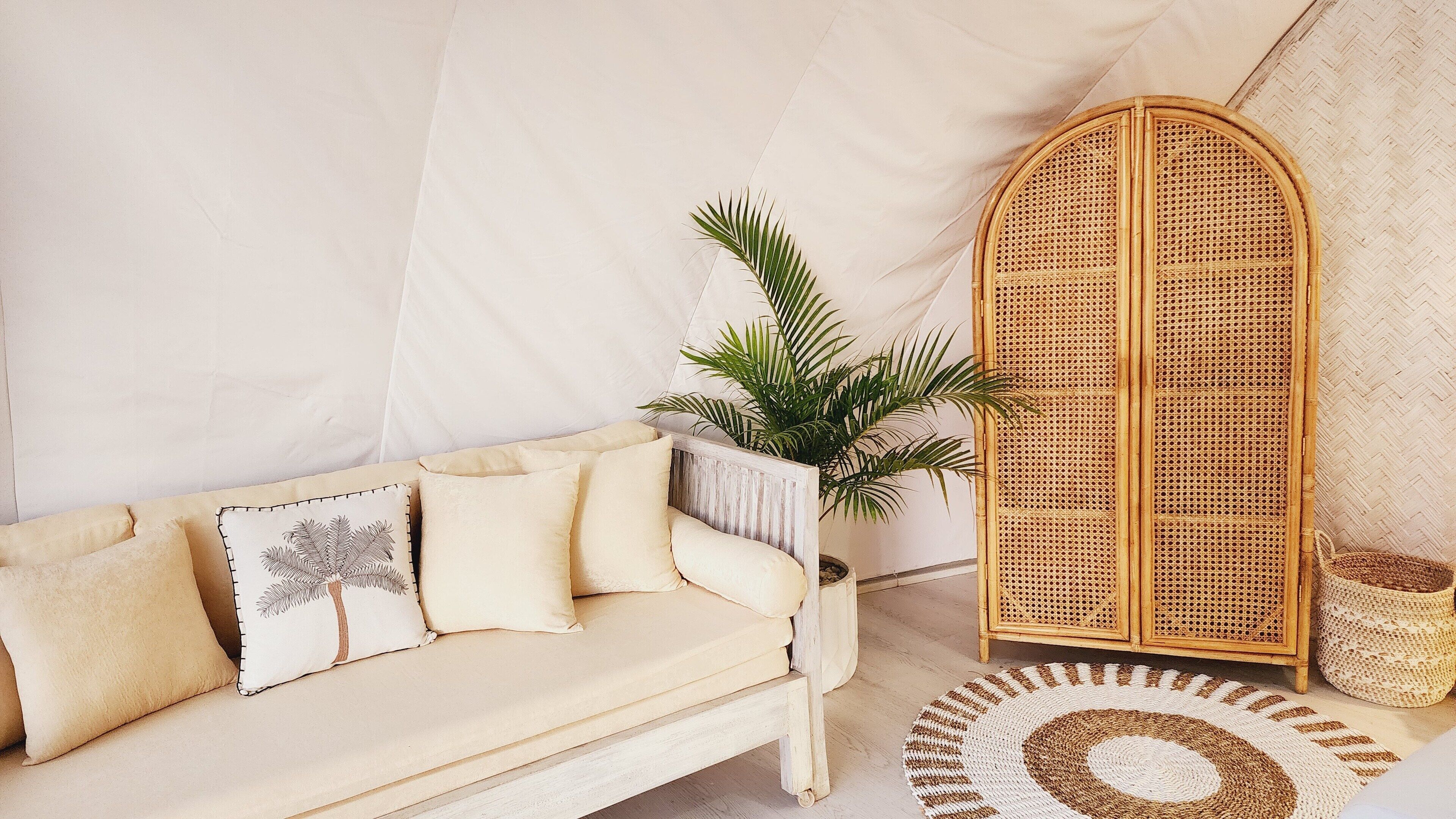 A cozy room with a beige sofa, a rattan cabinet, a potted plant, and a woven rug.