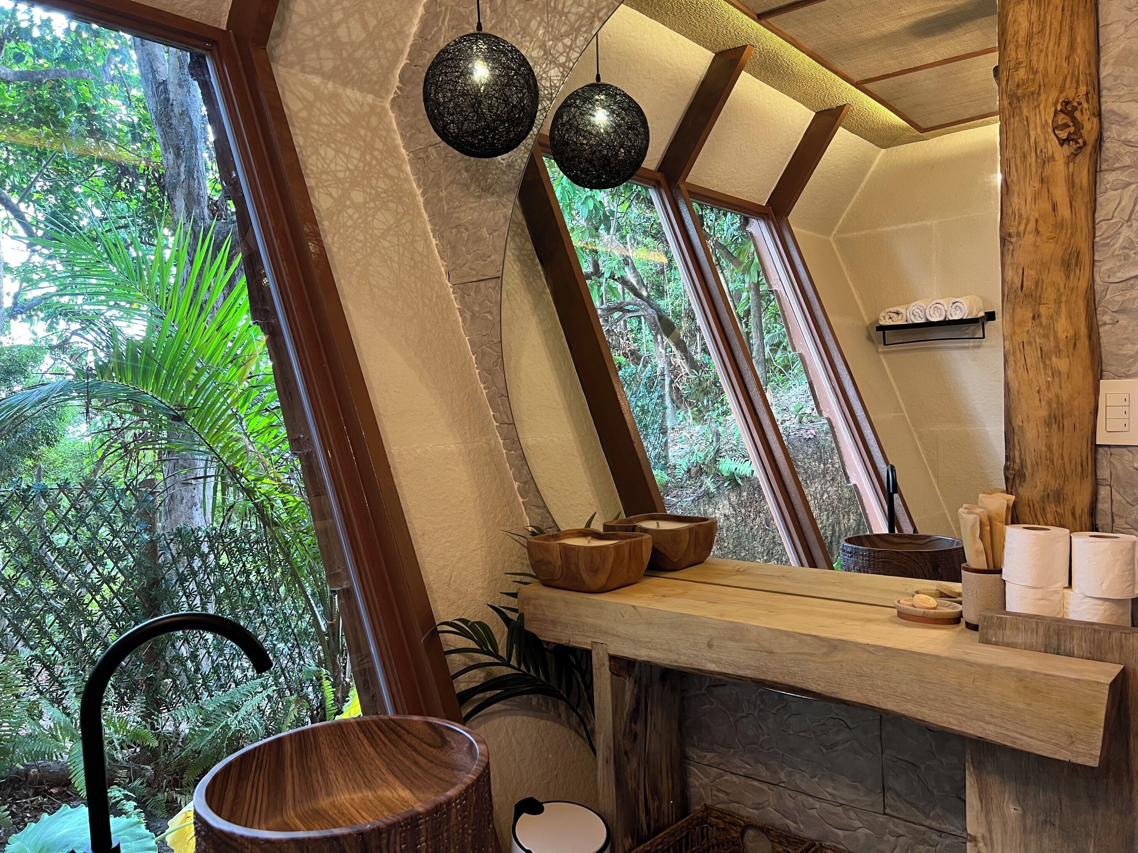 Une pièce dotée d’un plafond en pente, de poutres en bois, d’un comptoir en bois où sont disposées des serviettes et des articles de toilette, et de grandes fenêtres donnant sur un paysage verdoyant.