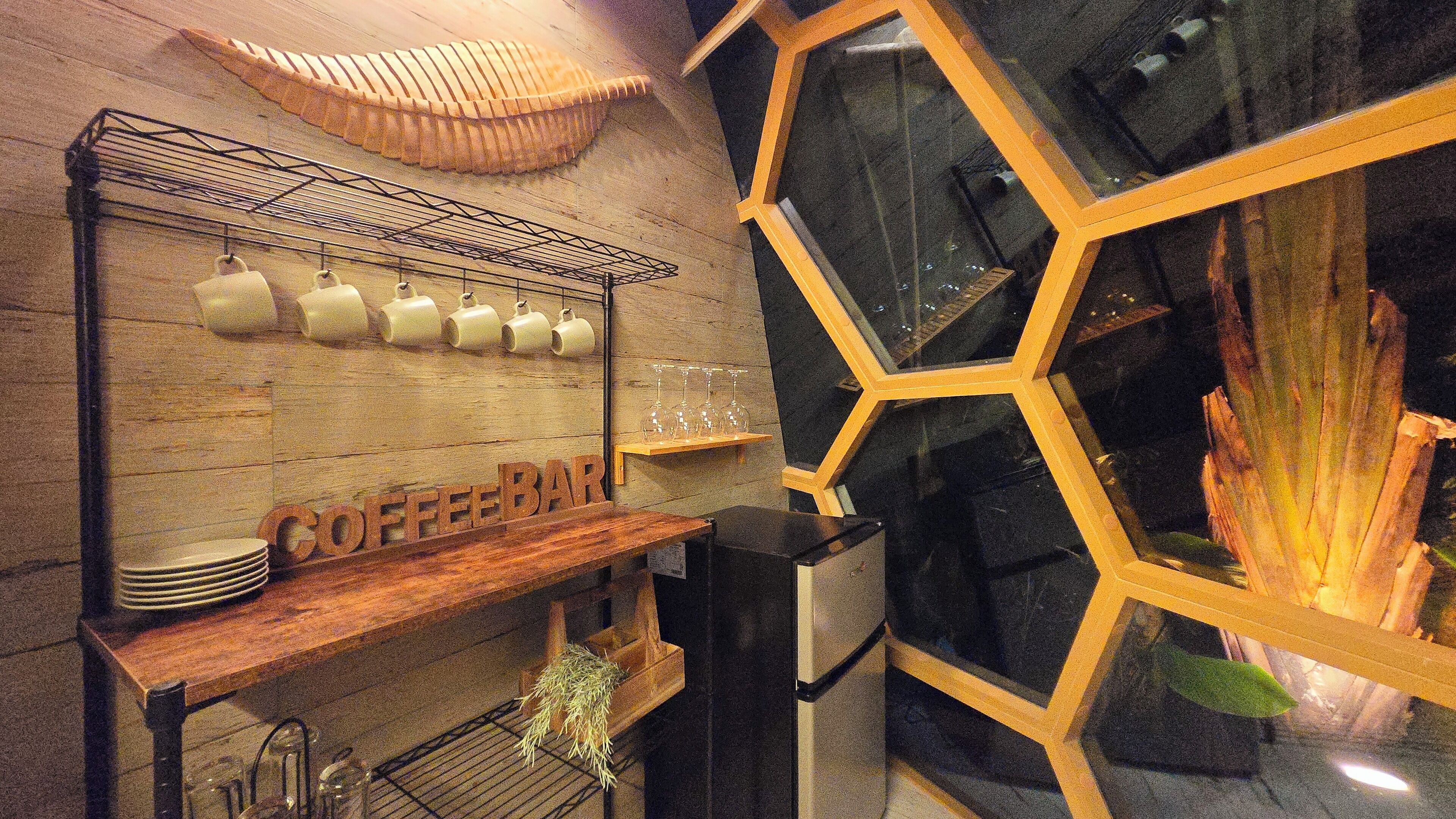 A coffee bar with a wooden shelf displaying mugs and glasses, and a sign that reads "COFFEE BAR".