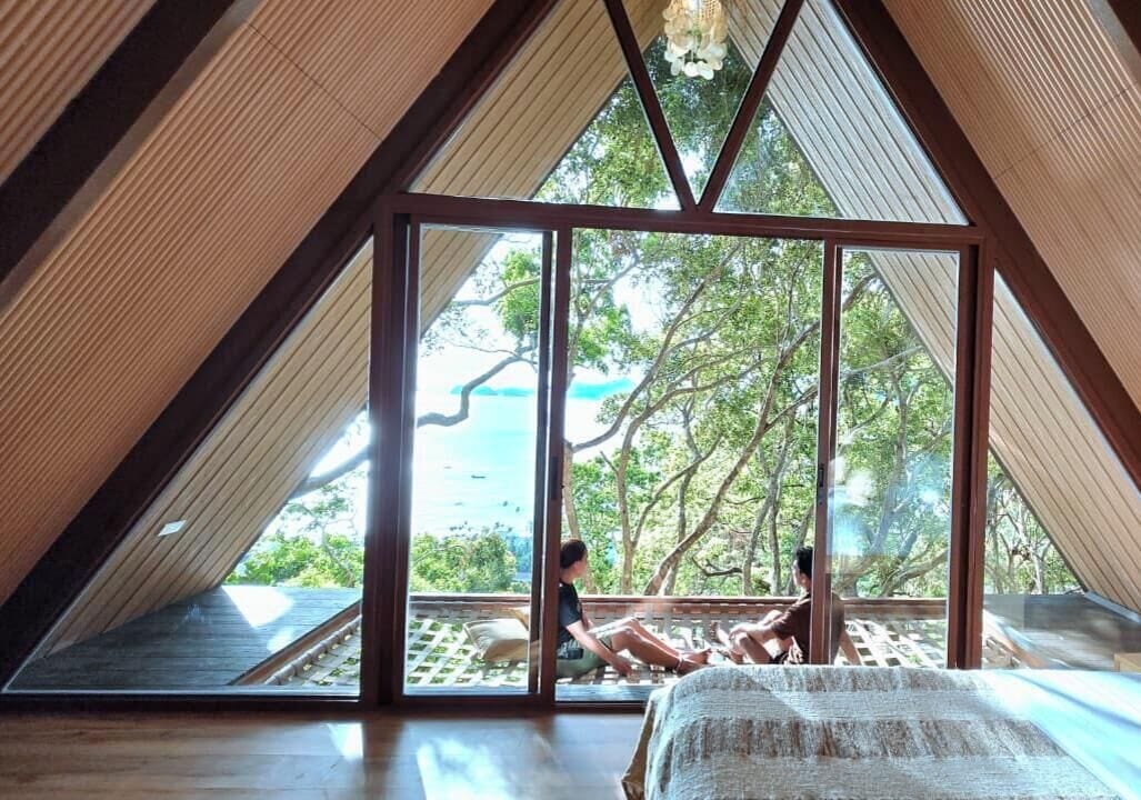 A room with a sloped ceiling and large windows, offering a view of the outdoors.