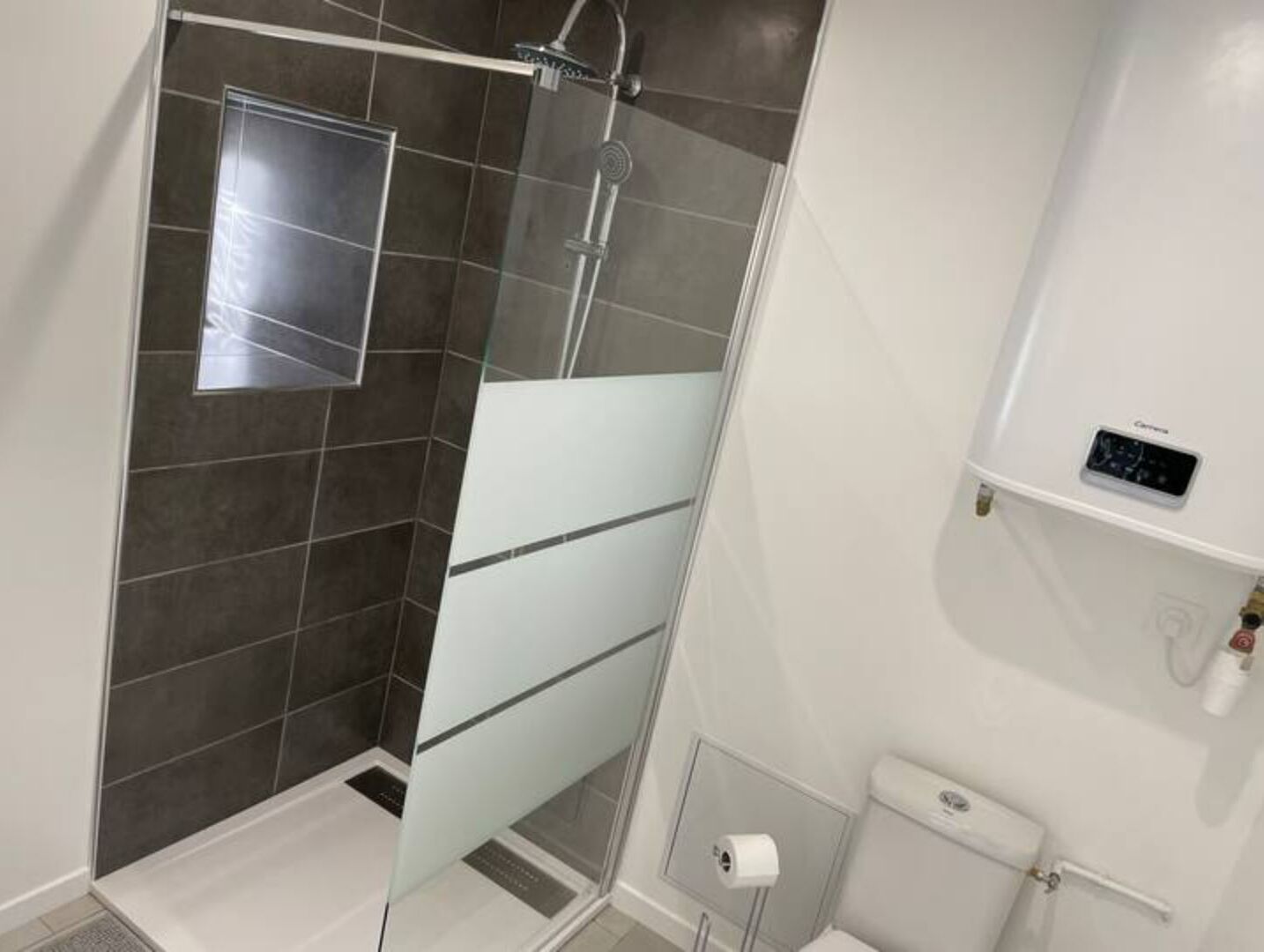 Een moderne badkamer met een douchecabine van glas, een toilet en een klein schap met een bedieningspaneel.