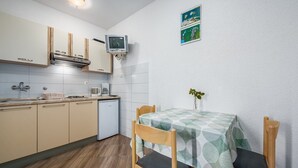 A compact kitchen with a dining area, featuring a small refrigerator, a microwave, and a television mounted on the wall. - Little apartment near the beach - Aleks 3 (Umag)
