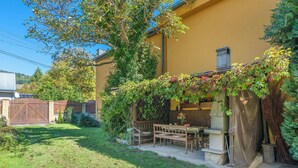 Un espace patio avec une table et des chaises, entouré de verdure et bordé d’un bâtiment jaune.