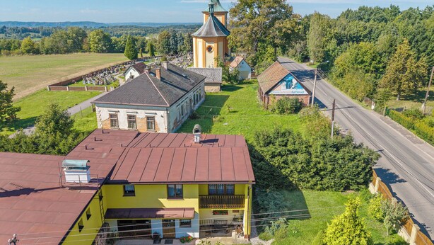 Un bâtiment jaune avec un toit rouge, une église avec un clocher vert et une route traversant un paysage rural.