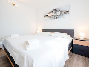 A modern hotel room with a neatly made bed, a bedside table with a lamp, and a wall-mounted abstract art piece.