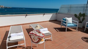 A terrace with two sun loungers, a table with a hat and a basket, and a cactus plant.
