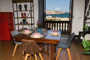 A dining area with a view of the sea, a red refrigerator, and a wooden table set for two. - Le Maree Deluxe Apartment by Dimore Trinacria - Sea View (Siracusa)