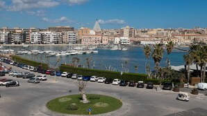 A marina with boats, a parking lot, and a cityscape with buildings and palm trees.