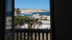 An open door leading to a balcony with a view of a coastal cityscape, including buildings and a marina.
