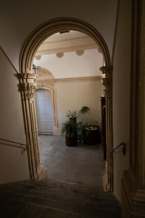 Una imponente escalera conduce a un espacio con un amplio ventanal, una puerta y una planta en maceta.