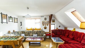 Un salon chaleureux avec un baby-foot, un canapé rouge et un divan à motifs.