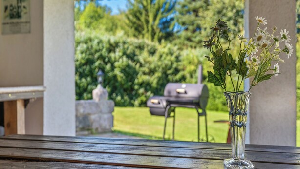 Un banc en bois, un vase en verre transparent contenant des fleurs, un barbecue et une statue en pierre, le tout dans un jardin.